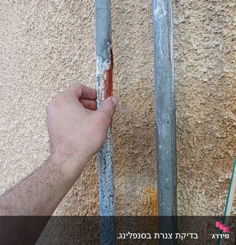 יד מחזיקה צינור מתכת חלוד על קיר